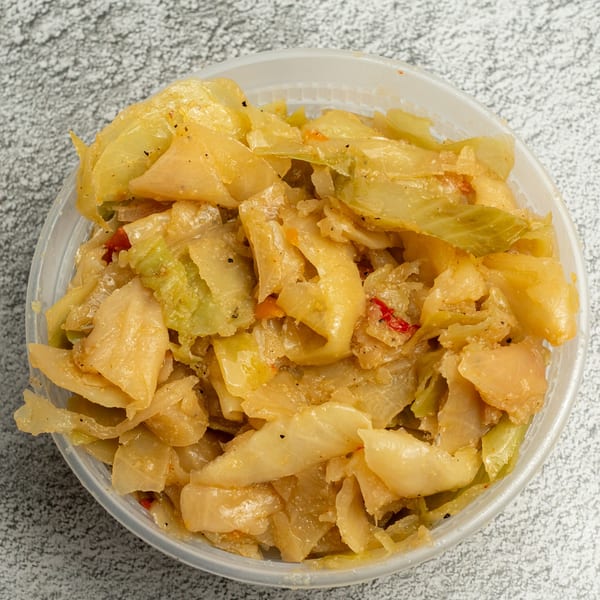 A clear plastic container filled with Angie's Soul House's seasoned, cooked cabbage, with hints of red pepper.