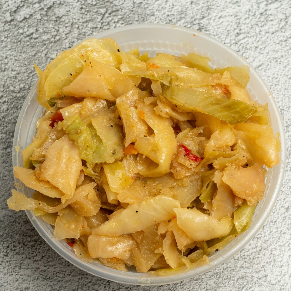 A clear plastic container filled with Angie's Soul House's seasoned, cooked cabbage, with hints of red pepper.