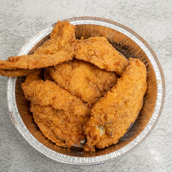 Golden-brown fried chicken pieces, seasoned with pepper, in a round aluminum takeout container.
