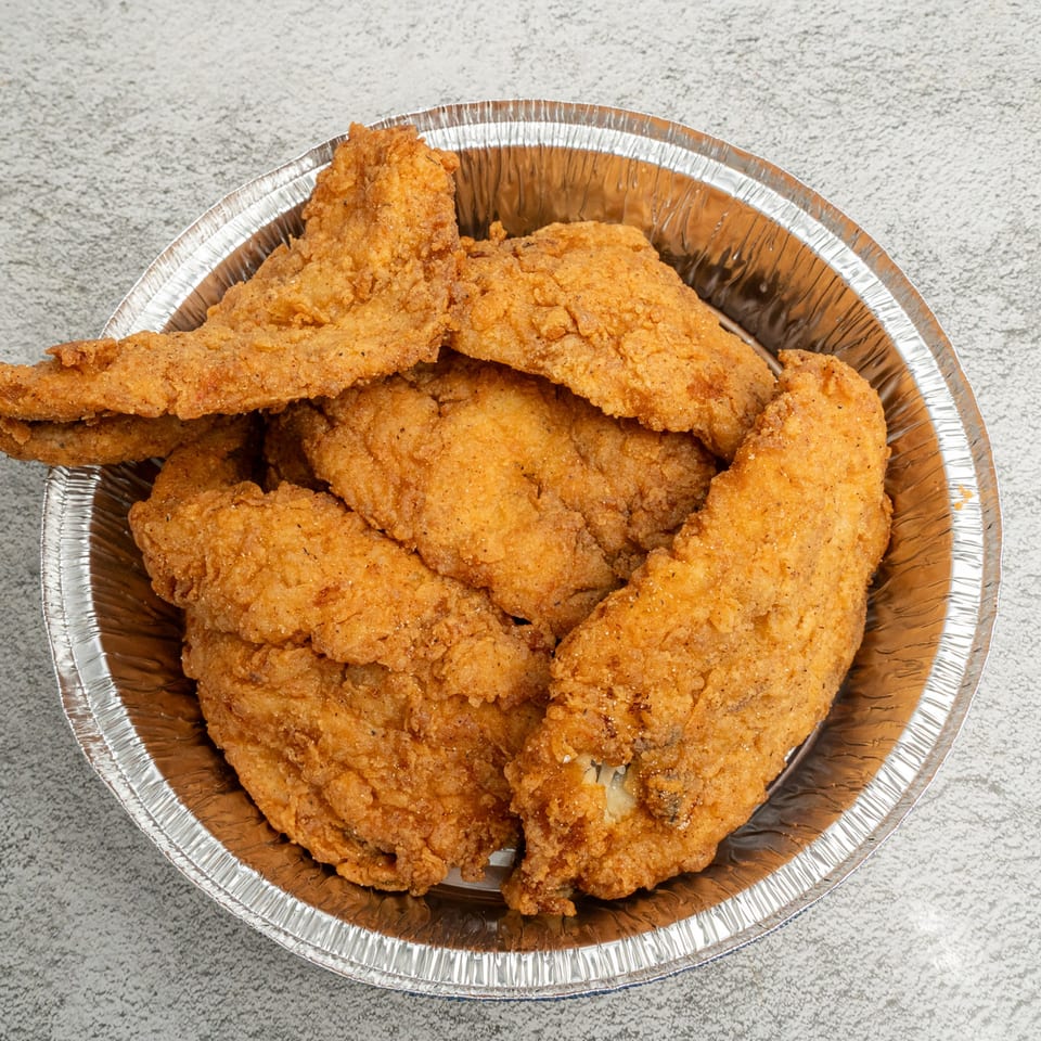 Golden-brown fried chicken pieces, seasoned with pepper, in a round aluminum takeout container.